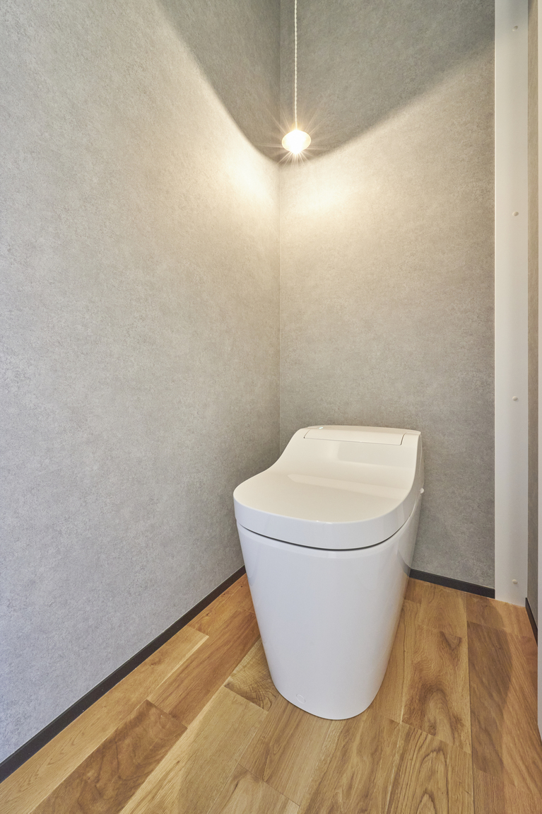 木床とグレーの壁。白のトイレがよく映える。ちいさなランプのかわいらしさが引き立ち、こまめに掃除もしやすいシンプルなトイレ